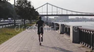 年轻的职业运动员早上沿着城市长廊在河边跑步。 活跃强壮的人做早操。 田径
